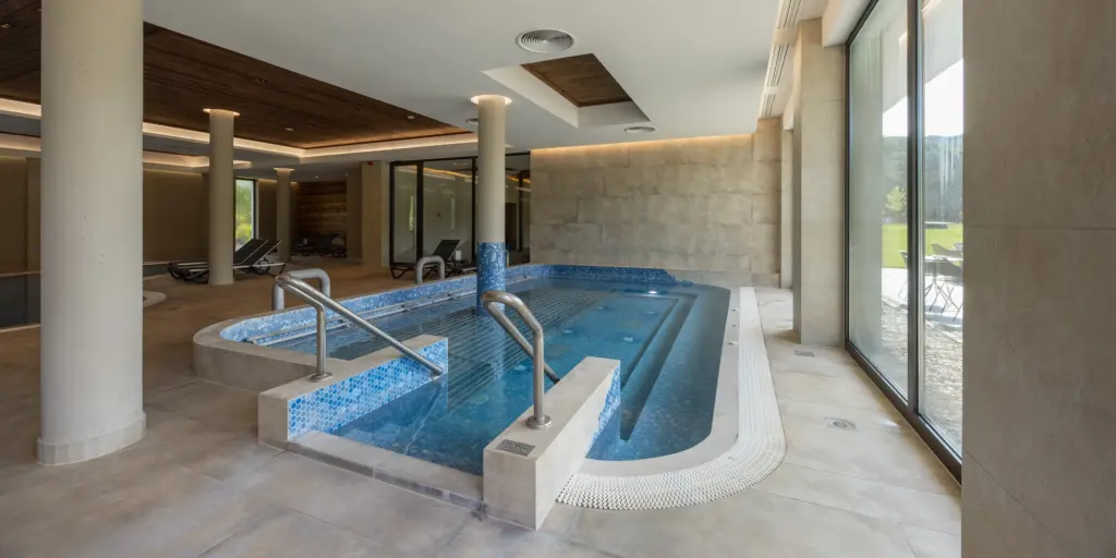 Luxuriöser Spa-Bereich mit Innenpool, Whirlwanne und Liegestühlen, umgeben von modernen, eleganten Glaswänden.