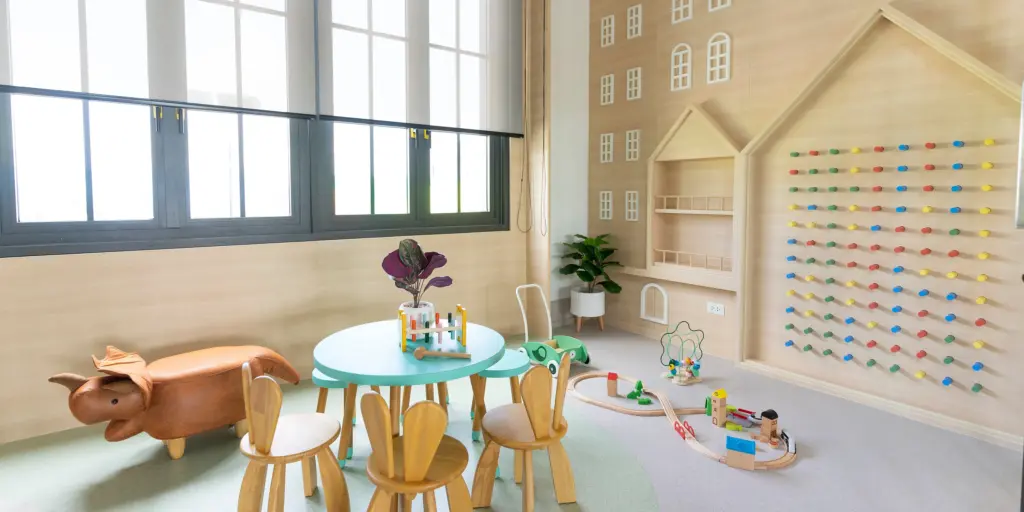 Helle Kinderspielecke mit buntem Tisch, Holzspielzeug, Tierhocker und kreativer Wandgestaltung.