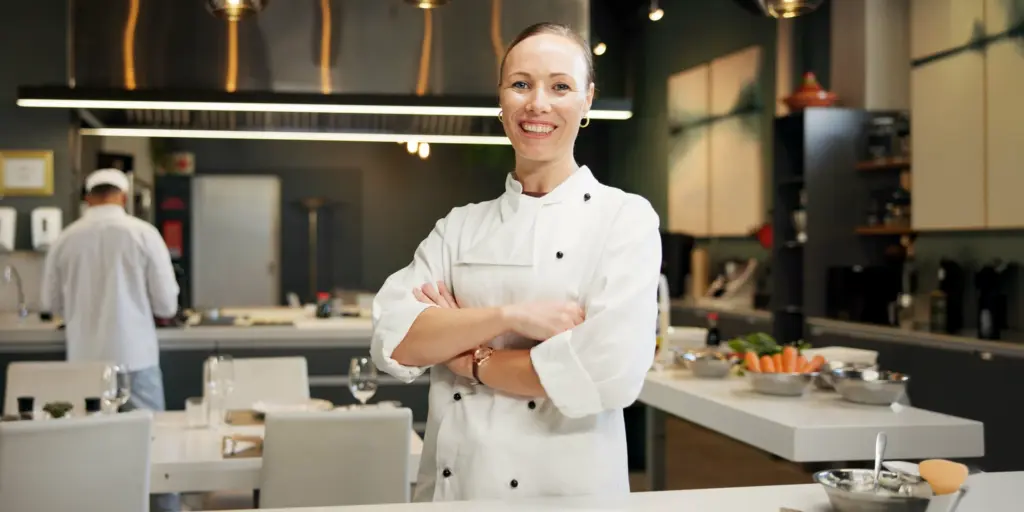 Eine lächelnde Chefköchin steht mit verschränkten Armen in einer modernen Küche.