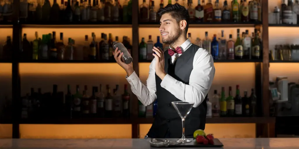 Barkeeper mit Fliege mixt Drink an gut bestückter Bar.