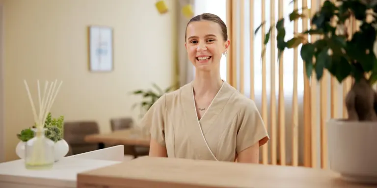 Eine lächelnde Frau in beiger Kleidung steht in einem modernen, natürlichen Innendesign.